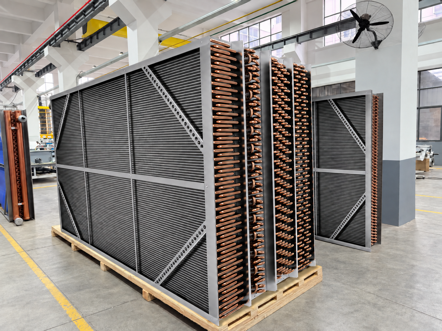 Coils comerciales grandes de climatización con aletas de aluminio expuestas y curvas de retorno de cobre, colocados sobre palés en una fábrica